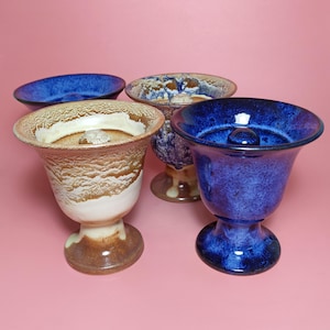 May include: Four ceramic cups with a footed base. Two cups are blue with a white glaze, and two cups are brown with a white glaze.