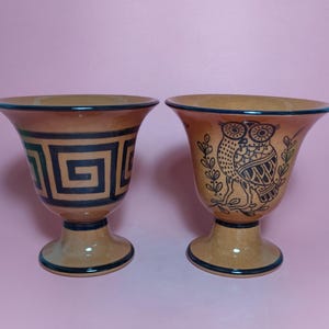 Könnte beinhalten: Zwei braune Keramikbecher mit einem Fuß. Ein Becher hat ein schwarzes und grünes geometrisches Design, der andere hat ein schwarzes und weißes Eulen-Design.