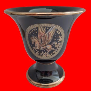 Peut inclure: Vase en céramique noire avec une bordure et une base dorées. Le vase présente une image dorée de Pégase, un cheval ailé, dans un design circulaire avec le mot "PEGASUS" écrit en or.