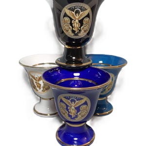 Könnte beinhalten: Drei Keramikvasen mit goldenen Verzierungen und einem Design mit einer geflügelten Figur. Die Vasen sind in Schwarz, Weiß und Blau.