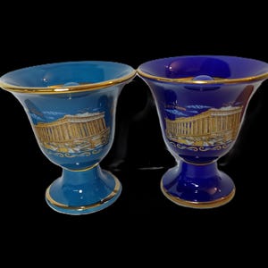 May include: Two ceramic cups with gold trim and a depiction of the Parthenon in Athens, Greece. One cup is blue and the other is teal.