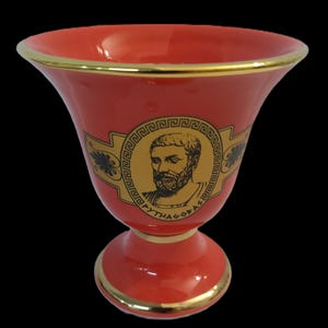 Könnte beinhalten: Roter Keramikbecher mit goldfarbenem Rand und einem goldenen Bild eines Männergesichts mit dem Text "PYTHAGORAS" um das Bild herum.