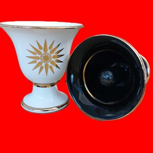 Puede incluir: Dos quemadores de incienso de cerámica, uno blanco con un diseño de sol dorado y otro negro con un borde dorado.