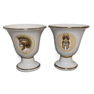 Könnte beinhalten: Zwei weiße Keramikbecher mit goldenen Verzierungen und einem goldenen Design eines römischen Helms auf jedem Becher.