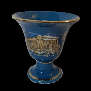May include: A blue ceramic vase with a gold rim and base. The vase features a gold illustration of the Parthenon on the front.