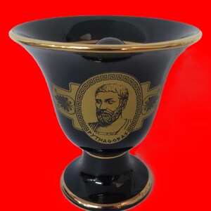Könnte beinhalten: Schwarze Keramikvase mit goldener Verzierung und einem goldenen Bild von Pythagoras mit dem Text "PYTHAGORAS" auf der Vorderseite.
