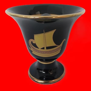 Könnte beinhalten: Schwarze Keramikvase mit goldener Verzierung und einem goldenen Bild eines Schiffes mit einem griechischen Schlüsselmuster.