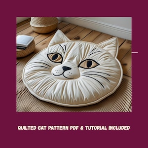 Peut inclure: Un coussin de sol en forme de chat, matelassé, de couleur crème. Le coussin présente des détails noirs pour les moustaches, les yeux et le nez. Le texte "QUILTED CAT PATTERN PDF & TUTORIAL INCLUDED" est en bas de l'image.