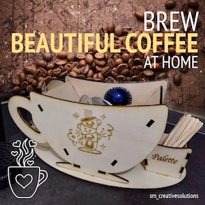 Op de afbeelding: Een houten organizer in de vorm van een koffiekopje met de tekst "BREW BEAUTIFUL COFFEE AT HOME". De organizer bevat koffiepads en roerstaafjes. Koffiebonen zijn op de achtergrond. Het ontwerp is een schattige stapel koffiekopjes.