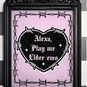 Op de afbeelding: Zwart ingelijste kunstdruk met een roze achtergrond. De print toont een zwarte hartvorm met prikkeldraad eromheen. De tekst "Alexa, Play me Elder emo" is geschreven in een gotisch lettertype.