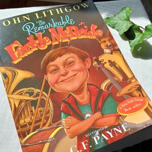 May include: A hardcover book titled "The Remarkable Farkle McBride" by John Lithgow. The cover illustration features a smiling boy with musical instruments in the background. A sticker indicates it's a New York Times bestseller.