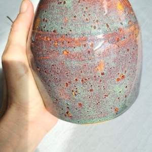Può includere: Un vaso in ceramica fatto a mano con una glassa macchiata. Il vaso presenta una miscela di colori, tra cui verde, marrone e arancione. Il vaso ha una forma arrotondata e una finitura lucida, perfetto per esporre fiori o come elemento decorativo.