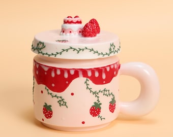 May include: A pink ceramic mug with a lid, decorated with strawberries and a small cake. The mug has a large, rounded handle and is adorned with red dripping accents and green vine details. The lid features a miniature cake and two strawberries.