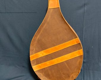 Könnte beinhalten: Eine braune Tennisschlägertasche aus Leder mit zwei orangefarbenen Lederriemen. Die Tasche hat einen braunen Ledergriff.