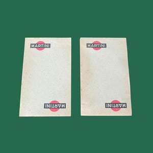 Könnte beinhalten: Zwei rechteckige Vintage-Martini-Untersetzer mit dem Martini-Logo in Rot und Weiß. Die Untersetzer sind beige und haben das Martini-Logo oben und unten aufgedruckt.