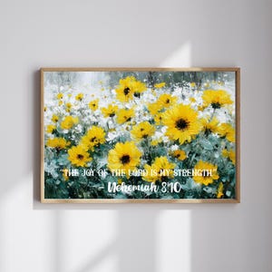 Op de afbeelding: Een ingelijste kunstdruk met een veld gele zonnebloemen en witte bloemen. Het kunstwerk bevat de tekst "THE JOY OF THE LORD IS MY STRENGTH" en "Nehemiah 8:10" in witte letters.