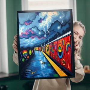 Puede incluir: Una impresión artística enmarcada que representa una colorida escena de metro bajo un cielo tormentoso con relámpagos. Los vagones del tren están decorados con formas geométricas vibrantes y diseños de arcoíris. La obra de arte tiene un estilo gráfico audaz.