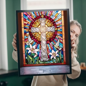 Puede incluir: Una ventana de vitral que representa una cruz blanca con palomas volando a su alrededor. La cruz está rodeada por un diseño de rayos de sol coloridos con piezas de vidrio rojo, amarillo, naranja, azul, verde y morado. La ventana está enmarcada en negro.