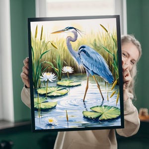 Puede incluir: Una pintura de acuarela de una garza azul de pie en un estanque con nenúfares y flores blancas. La garza tiene un cuello y un pico largos, y sus plumas son de un azul vibrante.