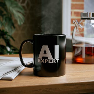 Peut inclure: Une tasse à café noire avec le texte "AI Expert" en lettres blanches. De la vapeur s'échappe de la tasse.
