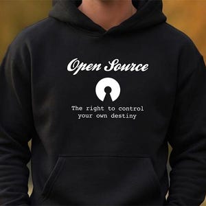 Könnte beinhalten: Ein schwarzer Kapuzenpullover mit dem weißen Schriftzug Open Source, einem weißen kreisförmigen Schlüsselloch-Symbol und dem weißen Text The right to control your own destiny auf der Brust. Das Kleidungsstück verfügt über eine Kängurutasche.