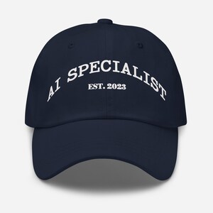 May include: A navy blue baseball cap with the text "AI SPECIALIST EST. 2023" in white, arched across the front. The cap has a curved brim and a rounded crown.