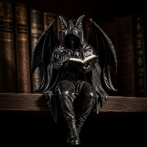 Peut inclure: Une figurine noire représentant une créature ailée et cornue vêtue d'une cape à capuche, assise en train de lire un livre ouvert. La silhouette possède de grandes ailes détaillées déployées et porte des bottes, le tout dans une finition sombre.