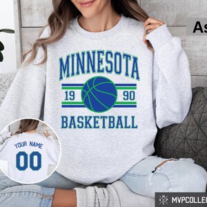 Pode incluir: Uma camisa de moletom cinza com o texto "Minnesota Basketball" em azul e verde. A camisa de moletom tem um gráfico de basquete com os números 19 e 90 de cada lado da bola.