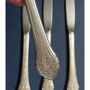 May include: Four silver dinner knives with ornate handles. The handles have a floral design.