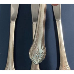 May include: Three silver flatware pieces with ornate handles. The handles have a floral design.