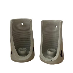 May include: A pair of white ceramic wall candle holders with a textured, ribbed design. Each holder has a small hole at the top for hanging and a circular indentation for a candle.