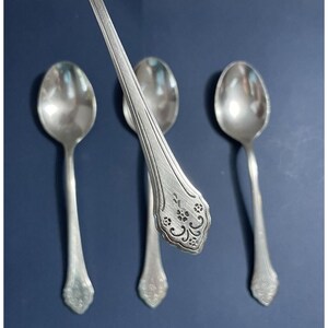 May include: Three silver spoons with ornate handles. The spoons have a floral design on the handle and a rounded bowl.