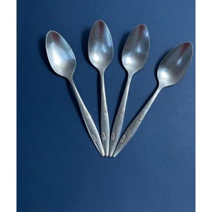 May include: Four silver spoons with a floral design on the handle. The spoons are arranged in a fan shape on a blue background.