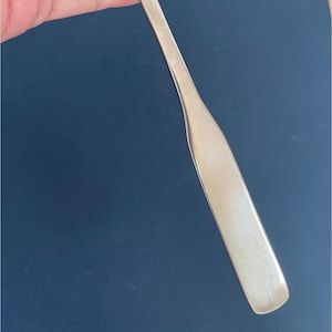 May include: A silver serving spoon with a long, narrow handle.