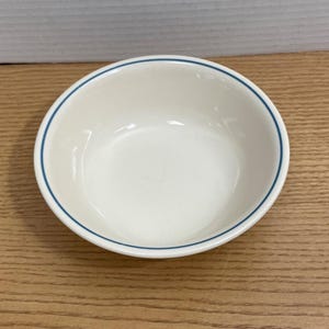 May include: A white ceramic bowl with a blue rim. The bowl is round and has a simple, classic design. This bowl is suitable for serving soups, cereals, or other dishes.