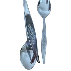 May include: Two silver spoons with a floral rose design. One spoon has a twisted handle, and the other has a straight handle. The spoons are made of a shiny, reflective metal.