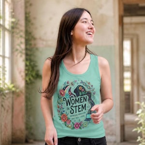 Könnte beinhalten: Hellblaues Tanktop mit einem farbenfrohen Aufdruck mit der Aufschrift "WOMEN IN STEM" in Weiß. Die Grafik zeigt eine Frauensilhouette, eine Rakete, DNA-Stränge und Blumen. Das Tanktop ist aus einem weichen Material.