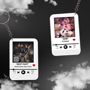 May include: Two white rectangular keychains with silver chains. Each keychain features a different image and text. One keychain displays a photo with the text "BEST PART" and the artist's name. The other keychain shows a photo with the text "4AM".