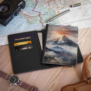 May include: Black leather passport holder featuring a mountain landscape design. The holder is open, displaying a passport and credit cards. A watch, camera, and pen are also visible.