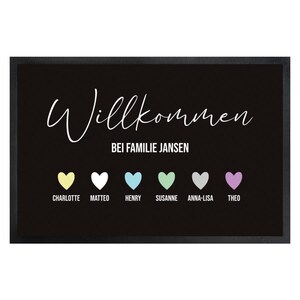 May include: Black doormat with white script reading "Willkommen" above "Bei Familie Jansen." Below are six colorful hearts with names: Charlotte, Matteo, Henry, Susanne, Anna-Lisa, and Theo. The mat has a black border.