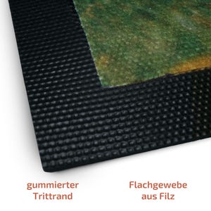 May include: Close-up of a black rubber doormat with a textured border and a green and brown felt insert. The doormat has the text "gummierter Trittrand" and "Flachgewebe aus Filz".
