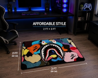 May include: A rectangular rug with a colorful shark design, measuring 2 ft x 3 ft. The rug features a black background with vibrant patches of blue, orange, yellow, and pink. The shark's mouth is open, revealing white teeth.