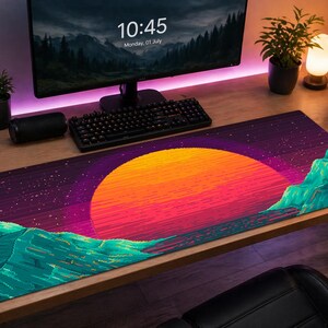 Pode incluir: Tapete de mesa retangular com um design de pôr do sol pixelizado, com um sol laranja vibrante, céu roxo e montanhas verde-azuladas. O tapete está em uma mesa de madeira com teclado e monitor.