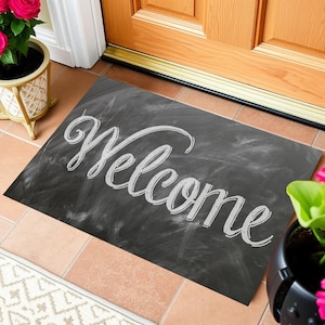 以下が含まれることがあります： 黒色のウェルカムマットに、白いチョーク風の文字で「Welcome」と書かれています。
