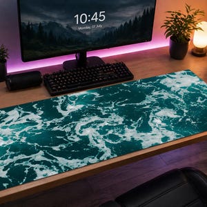 Può includere: Tappetino da scrivania rettangolare con un design a onde oceaniche turchesi e bianche. Il tappetino è su una scrivania di legno, con un monitor del computer, tastiera e altri accessori. Il tappetino misura circa 80 cm di lunghezza.