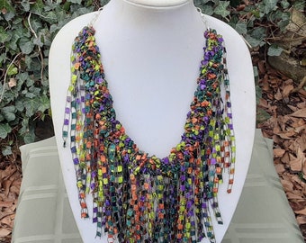 May include: A multi-colored crocheted necklace with a fringe of squares in shades of green, purple, orange, and black.