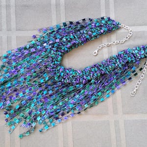 K&ouml;nnte beinhalten: Handgefertigte Halskette mit einzigartigem Design. Die Halskette hat eine lebendige Farbmischung, darunter Blau-, Lila- und Gr&uuml;nt&ouml;ne. Sie hat ein strukturiertes, fransiges Aussehen und wird durch eine silberne Kette akzentuiert.