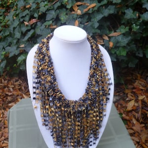 May include: A black and gold necklace made of crocheted yarn with a fringe design.