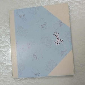 May include: A light blue book cover featuring cartoon bears and other characters. The word "tight" is written in pink script. The cover has a light beige border and a light beige triangle on the front.
