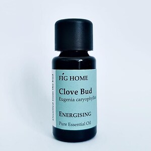 May include: A small, dark brown glass bottle with a black cap. The label reads "FIG HOME Clove Bud Eugenia caryophyllus ENERGISING Pure Essential Oil".